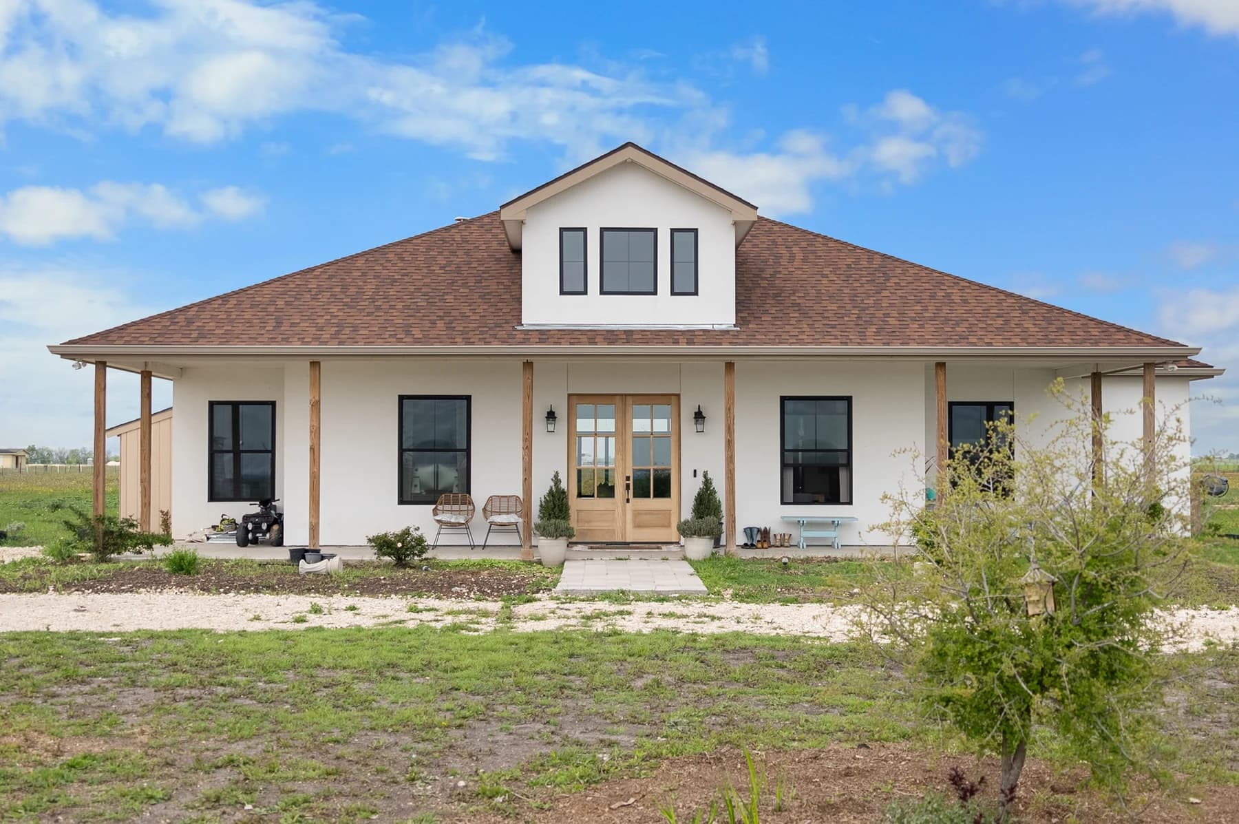 The completed white Plymouth custom home with a wraparound porch and black-framed windows
